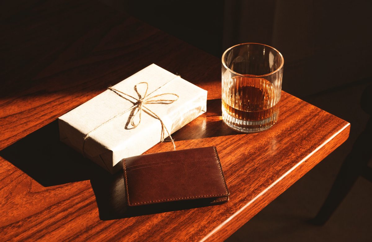 Geschenk in Kraftpapier mit Whiskyglas und Ledergeldbeutel auf dunklem Holztisch
