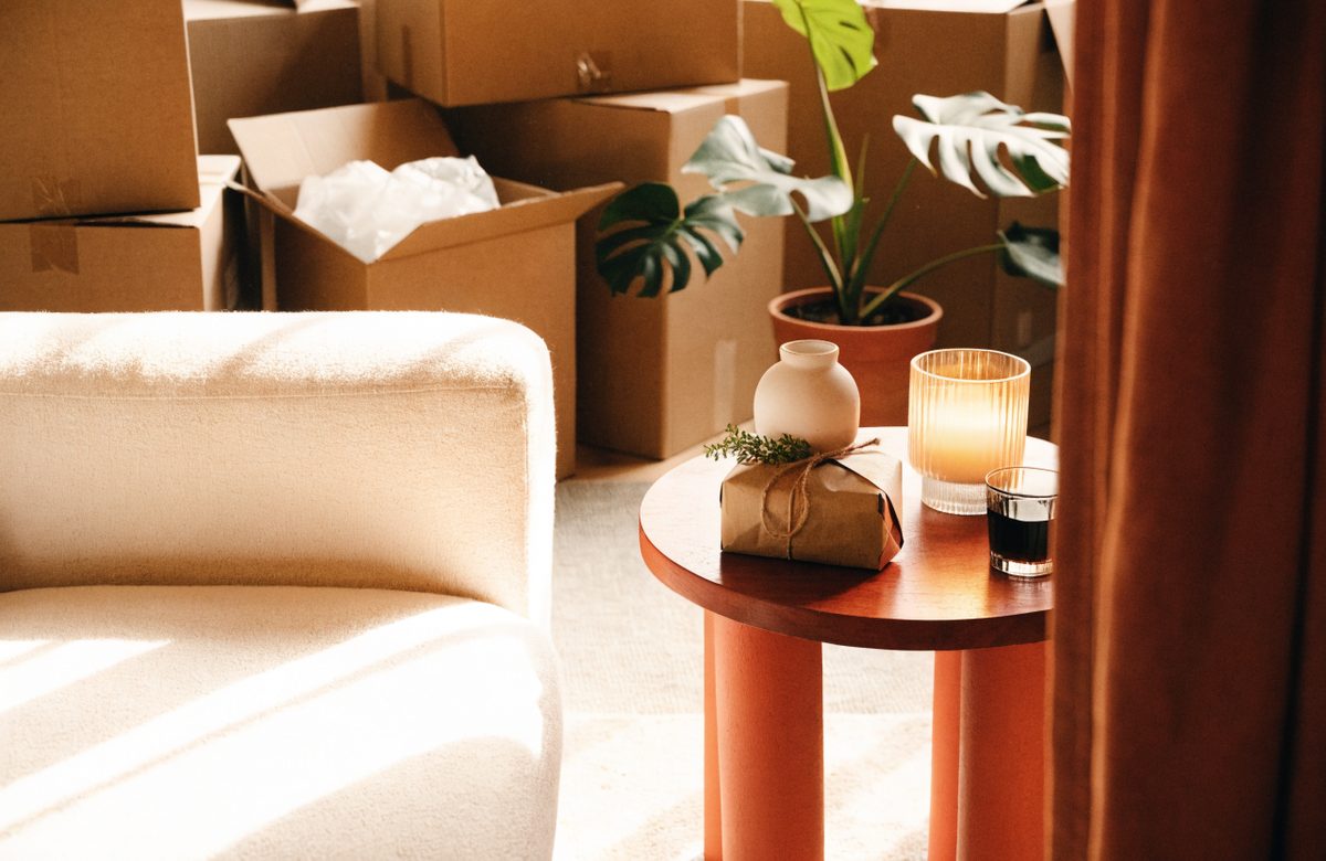 Einweihungsgeschenk mit Monstera, Kerze und Umzugskartons in neuer Wohnung